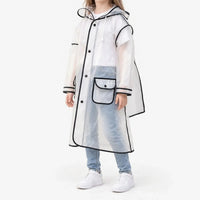 Side view of a girl in the frosted clear raincoat with black trim, snap buttons, a flap pocket and drawstring hood, with white sneakers. 2