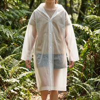 Child in a frosted white translucent hooded raincoat fastened with snap buttons, standing on a forest path among ferns. 1