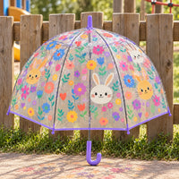 Clear dome umbrella with purple trim and handle, printed with bunny faces and colorful flowers, standing against a wooden fence outdoors. 1