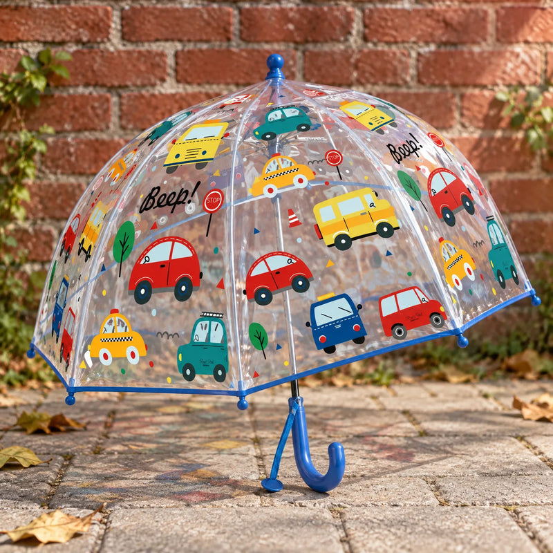 Clear dome umbrella with blue trim and handle, printed with colorful cars and buses, standing on paving stones in front of a brick wall. 3