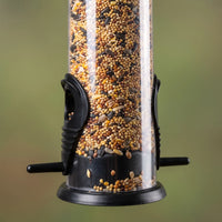 Close-up of the lower half of a seed-filled feeder with black base, feeding ports and perches against a blurred green background. 3