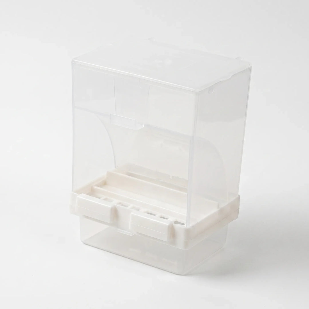 Angled view from the front showing the open feeding slot, the white base with two clip tabs and the clear tray below. 4