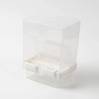 Angled view from the front showing the open feeding slot, the white base with two clip tabs and the clear tray below. 4