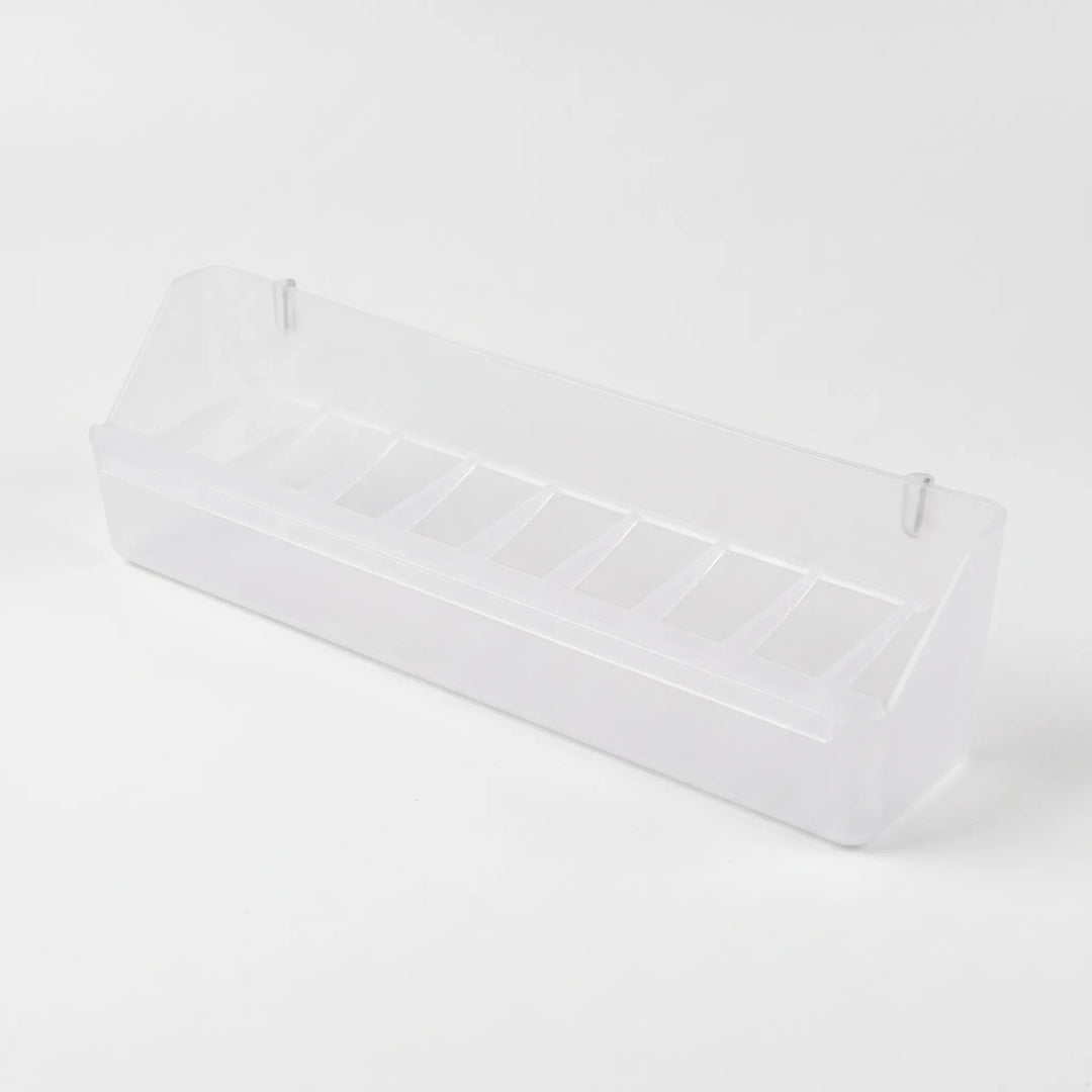 Angled view of the empty long clear feeder showing its row of small compartments and two hanging pegs. 7