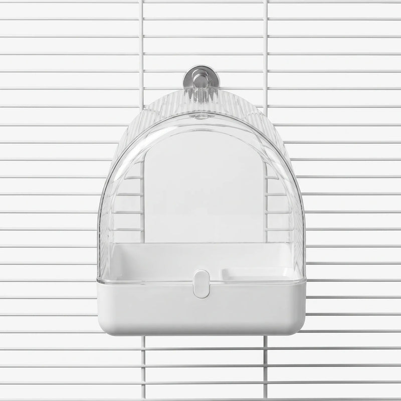 Front view of the arched clear bird bath with a white base and metal fixing peg, hung on a white cage. 1