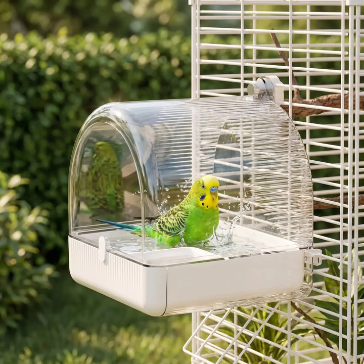 A green and yellow budgie splashing in the bath, which is attached to a white cage in a garden. 2