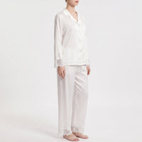 Three-quarter side view of the white satin pajamas worn by a model, showing the button front, chest pocket and lace-edged hems. 4