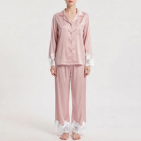 Front view of the pajama set in dusty pink satin with contrasting white floral lace on the sleeve cuffs, pocket and trouser hems. 7