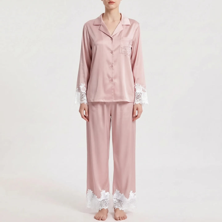 Front view of the pajama set in dusty pink satin with contrasting white floral lace on the sleeve cuffs, pocket and trouser hems. 7