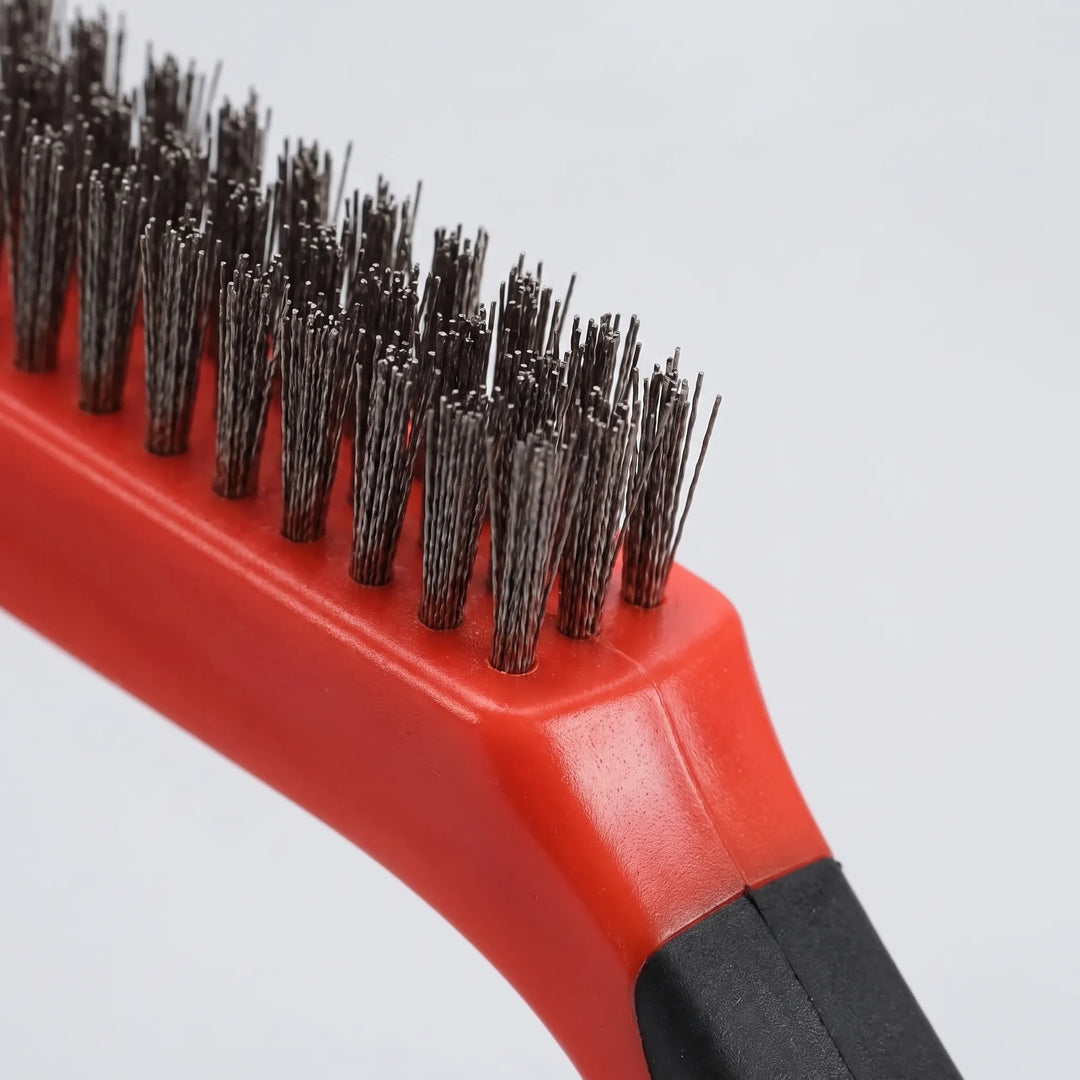Close-up of the red wire brush showing its dense metal bristles and black rubber-grip handle against a plain background. 3