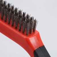 Close-up of the red wire brush showing its dense metal bristles and black rubber-grip handle against a plain background. 3