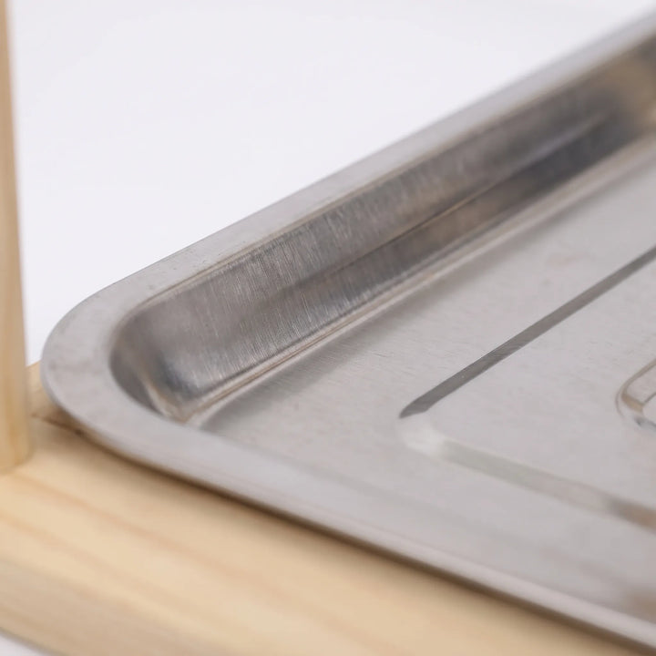 Close-up of the brushed stainless steel droppings tray with a rounded corner, resting on the pale wooden base. 3