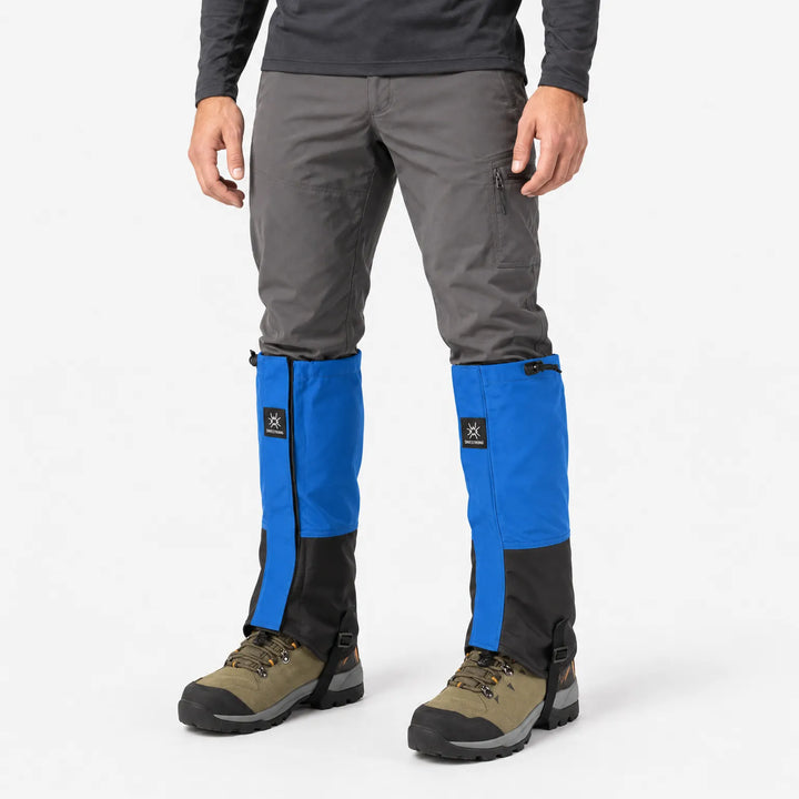 Man in grey trousers standing in blue and black gaiters over hiking boots, shown from a three-quarter front angle on white. 2