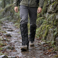 Hiker in black gaiters walking along a wet, muddy forest path, with water droplets beading on the fabric. 3