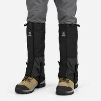 All-black gaiters with drawcord tops and ankle straps, worn over grey trousers and tan hiking boots, shown from the front. 8