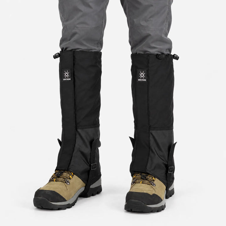 All-black gaiters with drawcord tops and ankle straps, worn over grey trousers and tan hiking boots, shown from the front. 8