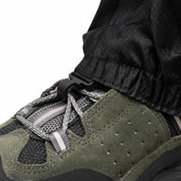 Close-up of the gaiter's lower hem with a plastic hook clipped to the laces of a green suede hiking shoe. 6