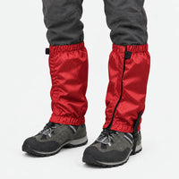 Red ripstop gaiters with elastic cuffs and a securing strap under the boot, worn with grey hiking shoes on white. 7
