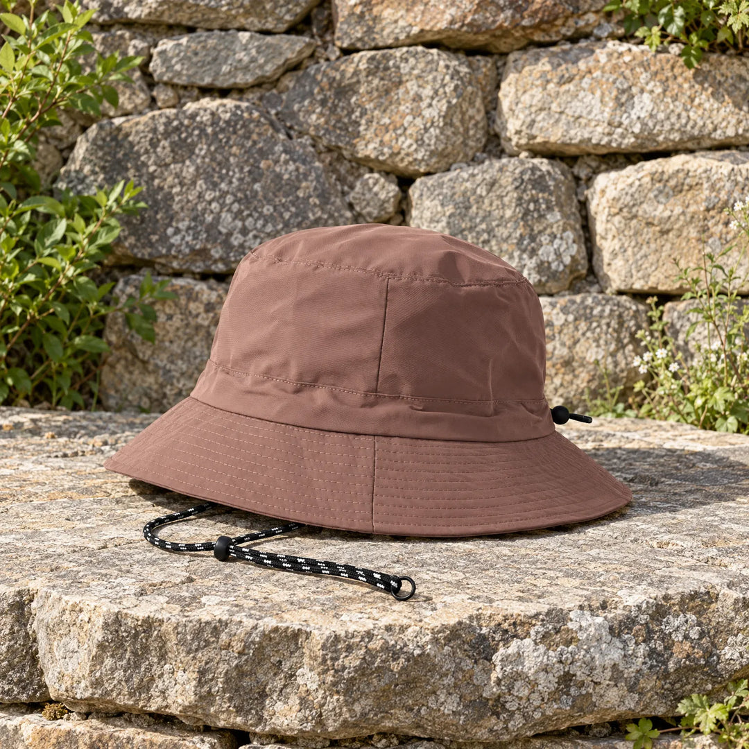 Brown bucket hat resting on a sunlit stone ledge, side view showing the stitched brim and drawcord with toggle. 3