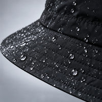 Close-up of a black hat brim and crown, water droplets beading on the stitched fabric. 6