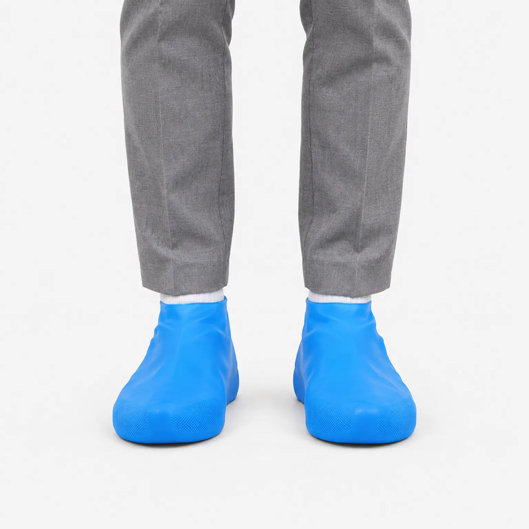 Front view of blue rubber shoe covers worn over shoes with grey trousers and white socks against a plain white background. 2
