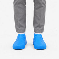 Front view of blue rubber shoe covers worn over shoes with grey trousers and white socks against a plain white background. 2