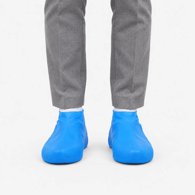 Front view of blue rubber shoe covers worn over shoes with grey trousers and white socks against a plain white background. 2