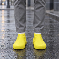Yellow rubber shoe covers worn on a wet city street, with water droplets beading on the surface and a rainy backdrop. 3