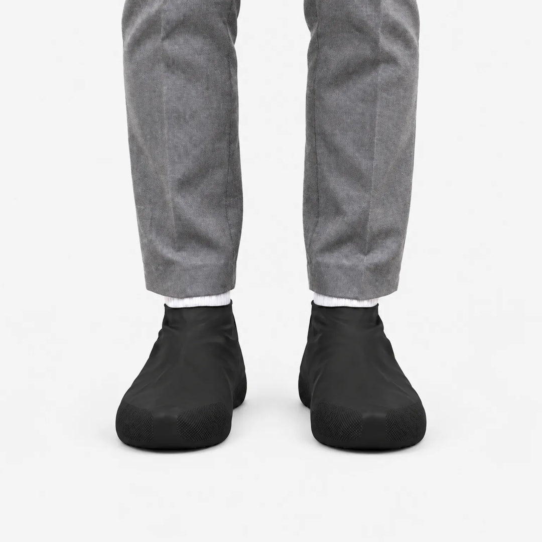 Front view of black rubber shoe covers worn with grey trousers and white socks, showing the textured grip at the toes. 4