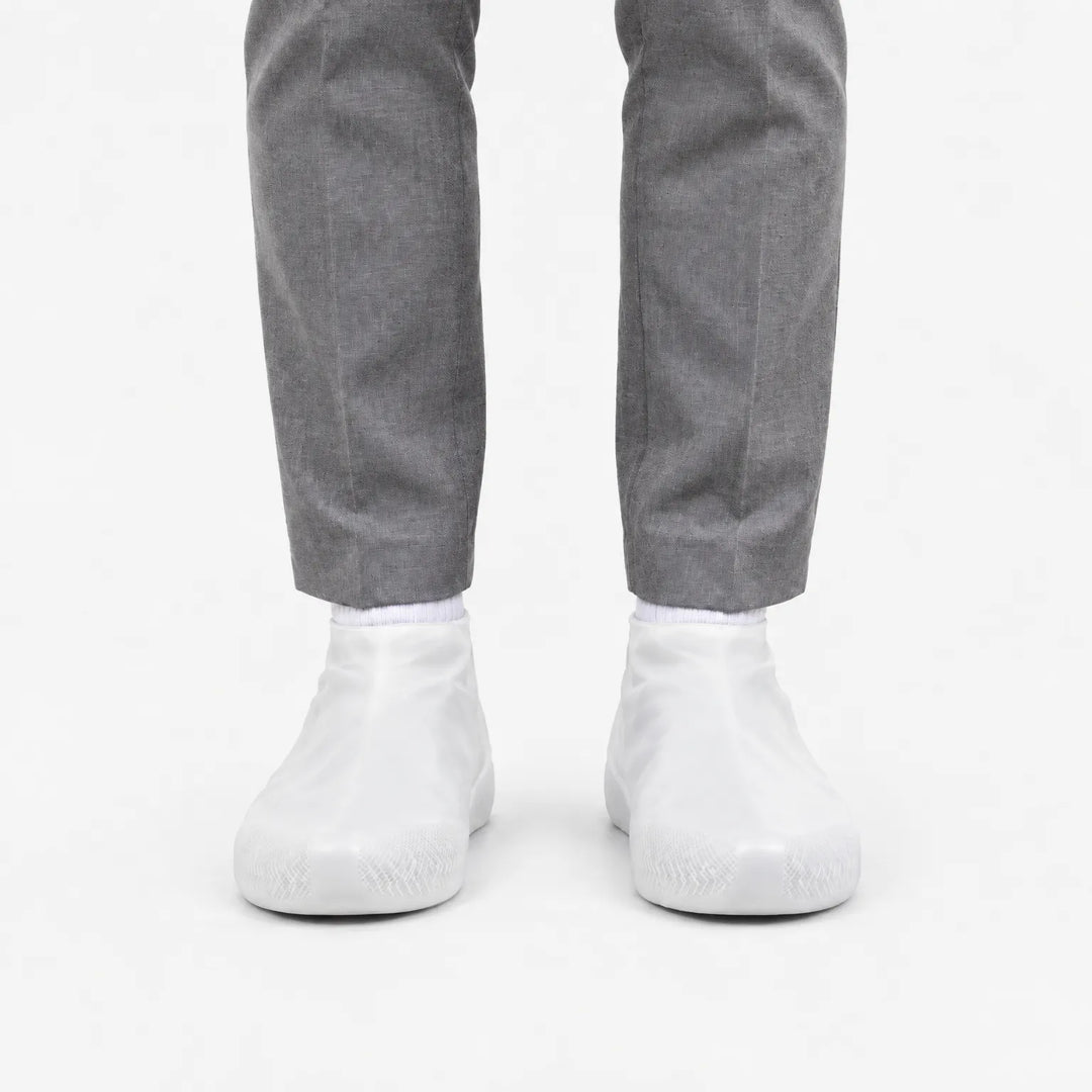 Front view of translucent white rubber shoe covers worn with grey trousers, with the grip texture visible on the toes. 8