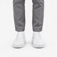 Front view of translucent white rubber shoe covers worn with grey trousers, with the grip texture visible on the toes. 8