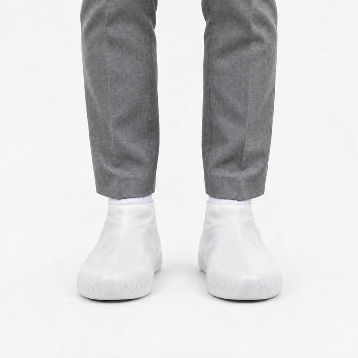 Front view of translucent white rubber shoe covers worn with grey trousers, with the grip texture visible on the toes. 8