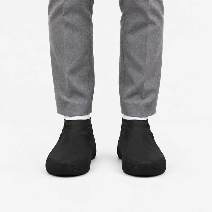 Another front view of black rubber shoe covers worn with grey trousers and white socks, with textured toe grip visible. 9