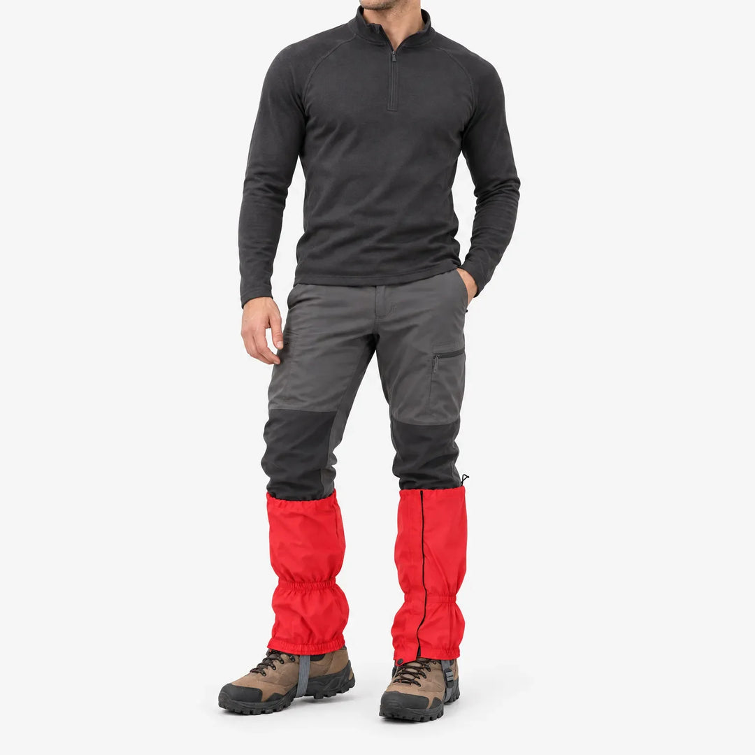 Full-length studio view of a man in a dark zip-neck top and grey trousers wearing red gaiters over brown hiking boots. 2