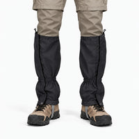 Front view of black gaiters worn over hiking boots with beige trousers, showing the front closure flap, snap fasteners and elastic cuffs. 9