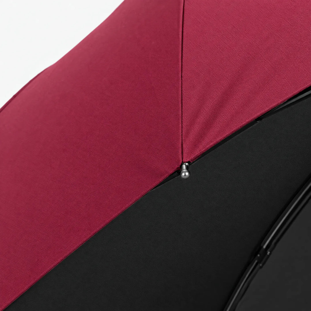 Close-up detail of a burgundy canopy seam with a small metal rib tip and black lining underneath. 4