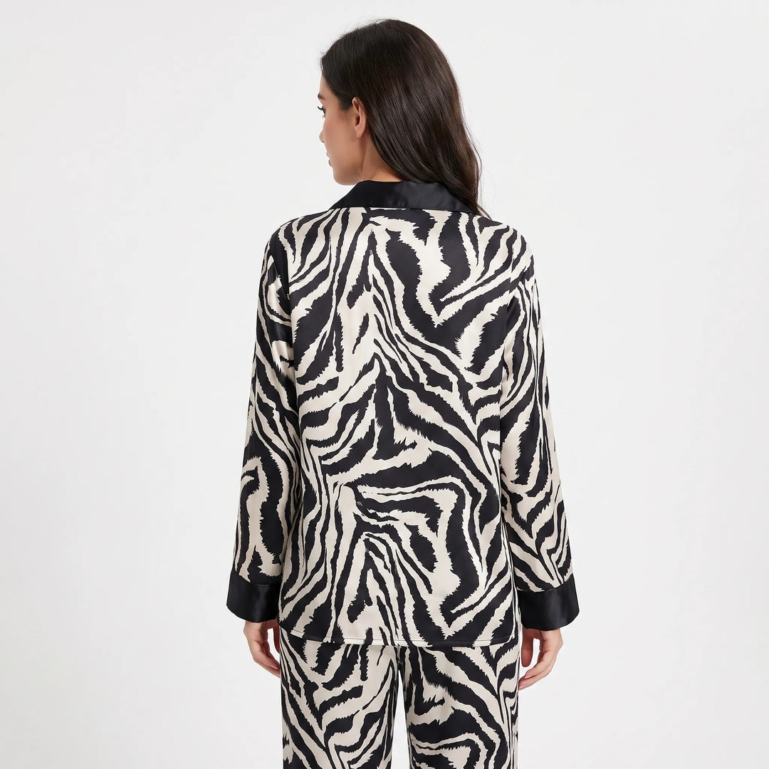 Back view of a woman wearing the long-sleeved zebra-print satin pyjama set, showing the continuous stripe pattern and black collar and cuffs. 2