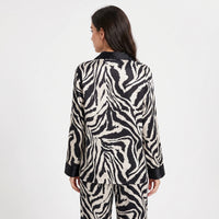Back view of a woman wearing the long-sleeved zebra-print satin pyjama set, showing the continuous stripe pattern and black collar and cuffs. 2