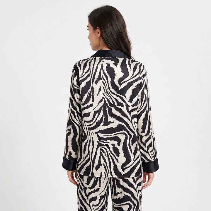 Back view of a woman wearing the long-sleeved zebra-print satin pyjama set, showing the continuous stripe pattern and black collar and cuffs. 2