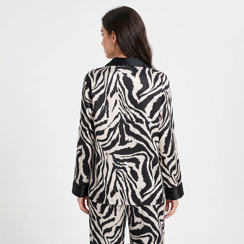 Back view of a woman wearing the long-sleeved zebra-print satin pyjama set, showing the continuous stripe pattern and black collar and cuffs. 2