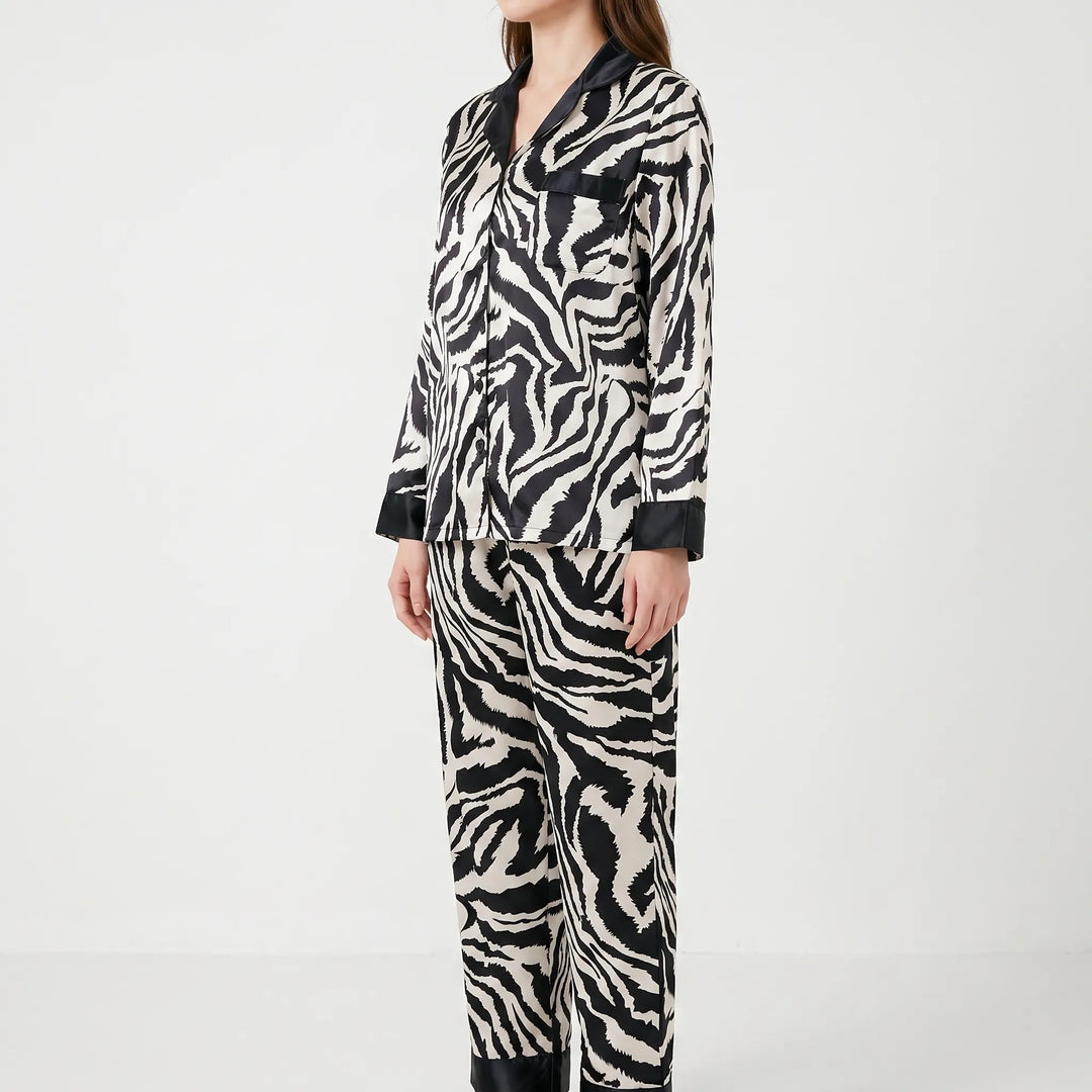 Side three-quarter view of a model in the long-sleeved zebra-print pyjama set with black-trimmed pocket, cuffs and trouser hems. 3