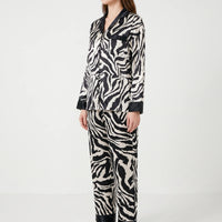 Side three-quarter view of a model in the long-sleeved zebra-print pyjama set with black-trimmed pocket, cuffs and trouser hems. 3