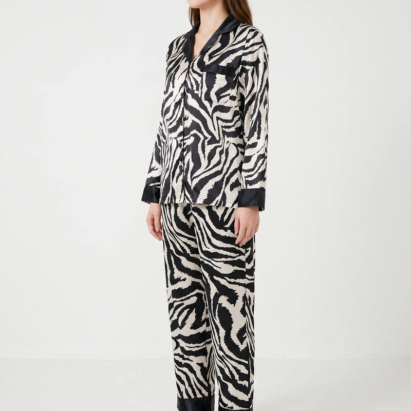 Side three-quarter view of a model in the long-sleeved zebra-print pyjama set with black-trimmed pocket, cuffs and trouser hems. 3