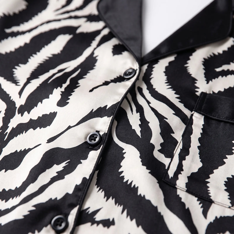 Close-up of the zebra-print satin fabric showing black buttons, black piped placket, notched collar and the corner of the chest pocket. 4