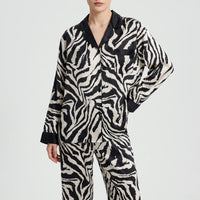 Front view of a model in the long-sleeved zebra-print pyjama shirt with black collar, buttons and pocket, worn with matching trousers. 6