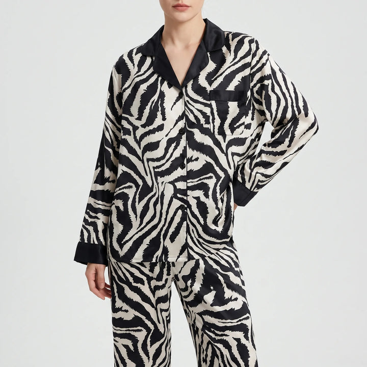 Front view of a model in the long-sleeved zebra-print pyjama shirt with black collar, buttons and pocket, worn with matching trousers. 6