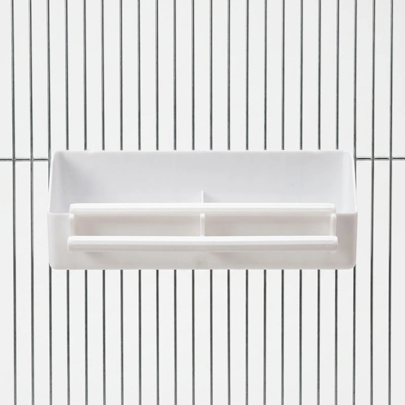 Front view of a white plastic two-compartment feeder with two perches, hung on the vertical bars of a metal cage. 1