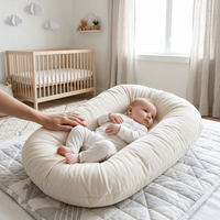 Cream lounger on a quilted play mat with a baby lying inside and a parent's hand resting on it 1