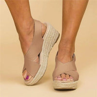 Front three-quarter view of taupe wedge sandals with crossed straps and woven jute soles, worn on feet 3