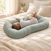 Baby asleep on its side in a sage green cushion on a cream bed 1